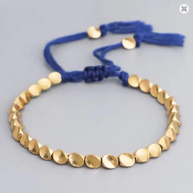 Gold beaded bracelet with blue cord on a light gray background