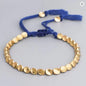 Gold beaded bracelet with blue cord on a light gray background