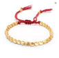 Gold beaded bracelet with a red string on a white background