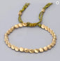 Gold beaded bracelet with green cord on a light gray background