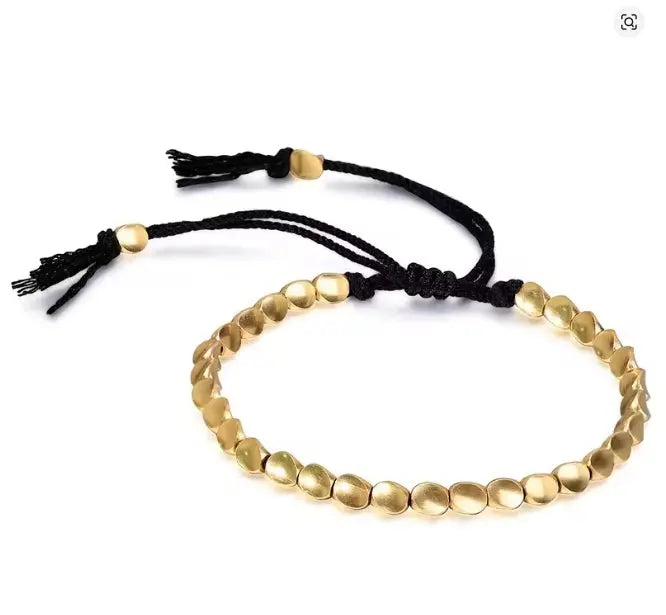 Gold beaded bracelet with black cord on a white background