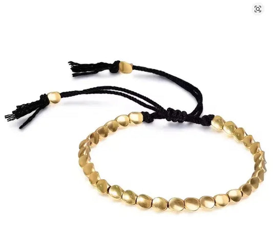 Gold beaded bracelet with black cord on a white background