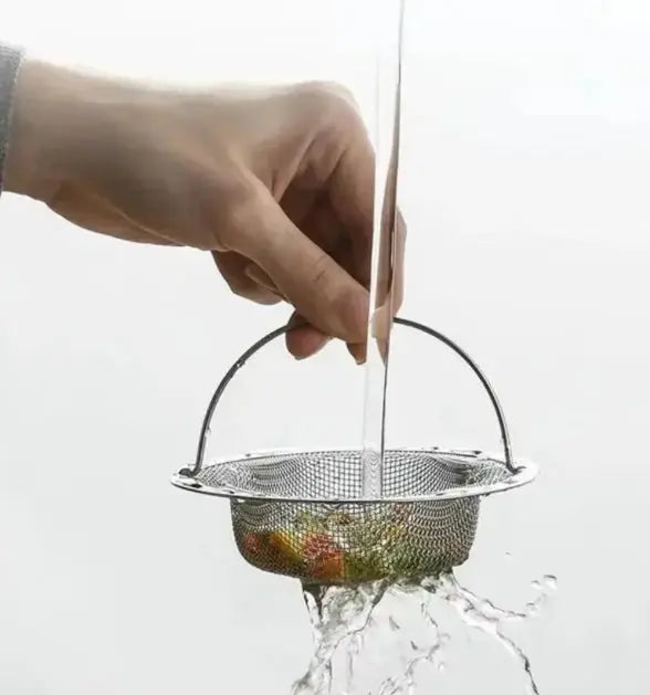 Hand holding a metal mesh strainer over a glass of water with fruits inside, on a white background.
