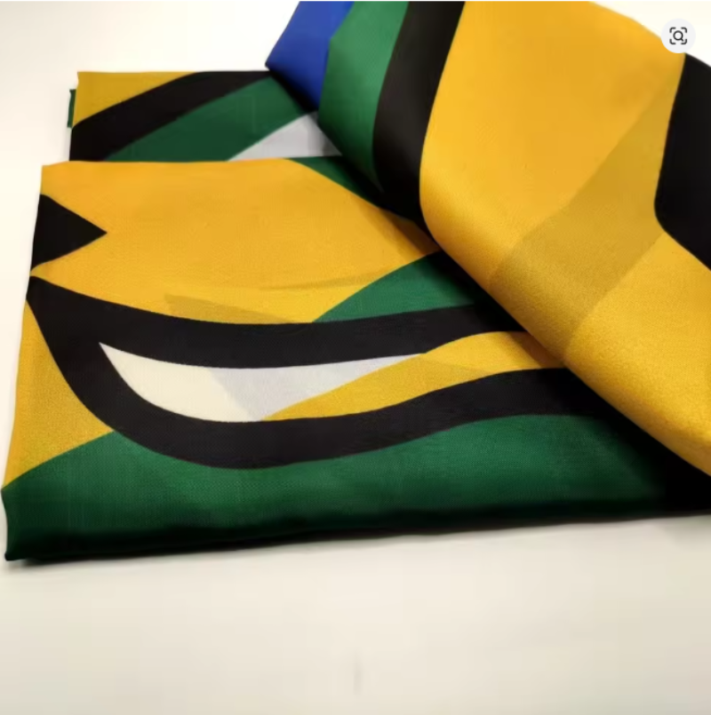 A folded and rolled fabric accessory, likely a scarf or pocket square, featuring a bold graphic print of the Jamaican flag with yellow, green, black, white, and blue sections.