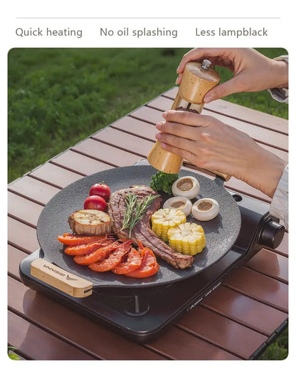 Person seasoning food on a portable grill with a view of grass in the background