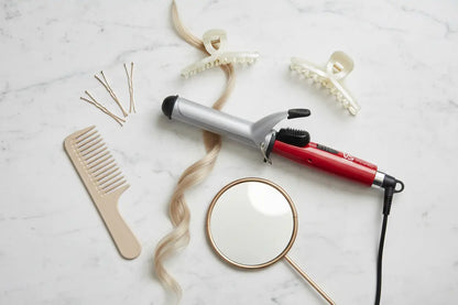 Hair styling tools including a comb, hair straightener, and hair curler on a marble surface.