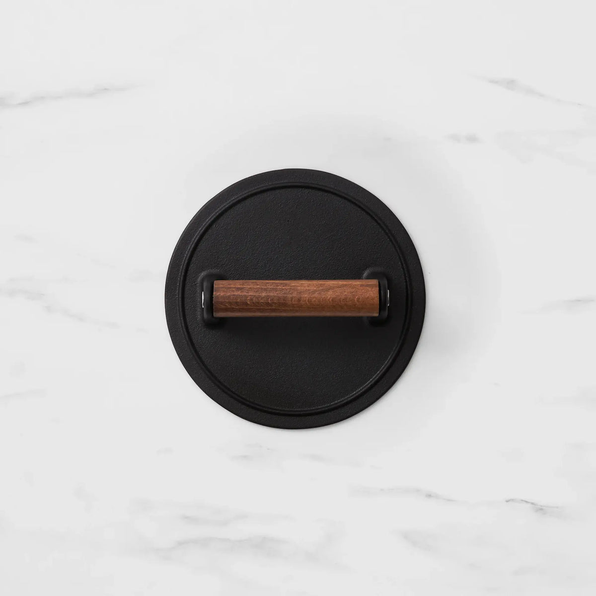 A round black metal wall hook with a horizontal wooden handle, shown from a top-down view on a white marble background.