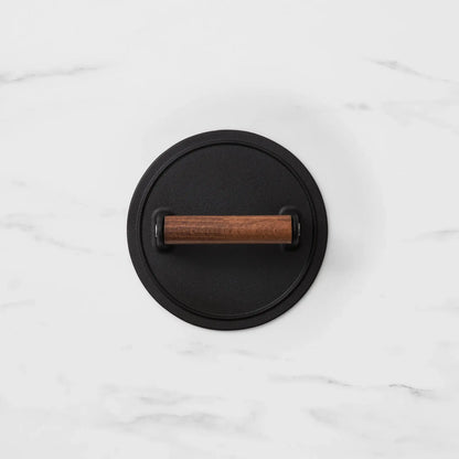 A round black metal wall hook with a horizontal wooden handle, shown from a top-down view on a white marble background.