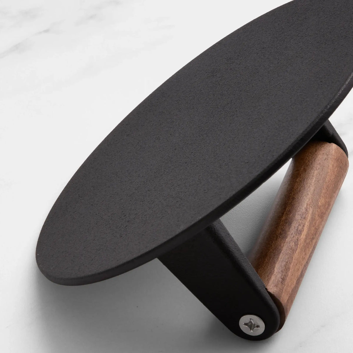 Close-up of a round pizza cutter with a matte black metal blade and a brown wooden handle, resting on a light marble surface.