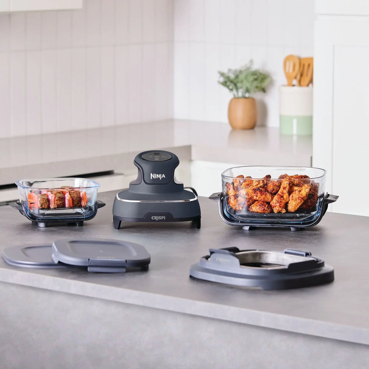 Ninja food dehydrator set with two glass baking dishes filled with food, a central dark gray dehydrator unit, and two gray lids on a kitchen countertop.