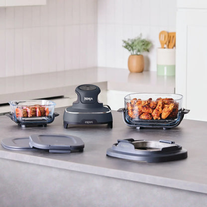 Ninja food dehydrator set with two glass baking dishes filled with food, a central dark gray dehydrator unit, and two gray lids on a kitchen countertop.