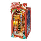 A Christmas-themed miniature city diorama set inside a decorative red box. The display features a detailed village scene with a lit Christmas tree, snowman, gift boxes, and festive decorations under a 'Merry Christmas' sign, shown against a plain white background.