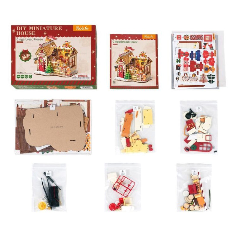 A DIY miniature house kit shown with its retail box, a smaller instruction card, a sticker sheet, and multiple clear bags containing wooden building pieces, decals, and accessories on a white background.