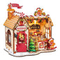 A detailed gingerbread-themed wooden toy house set with a bakery facade, decorated with gingerbread men figures, a small Christmas tree, candy cane accents, and warm glowing interior details, shown on a plain white background.