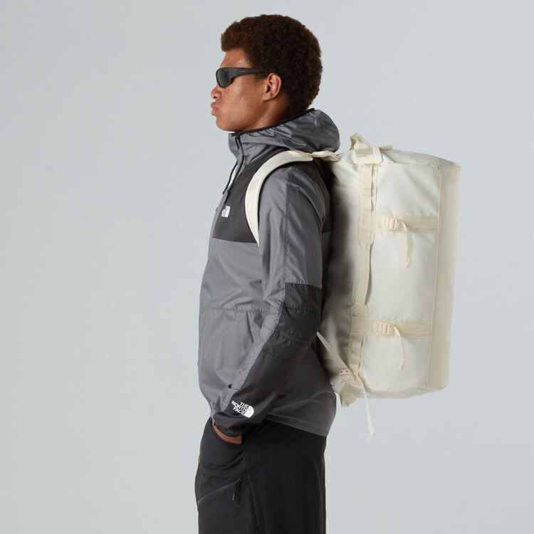 Person wearing a gray jacket and carrying a beige backpack against a light gray background