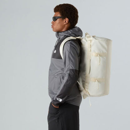Person wearing a gray jacket and carrying a beige backpack against a light gray background