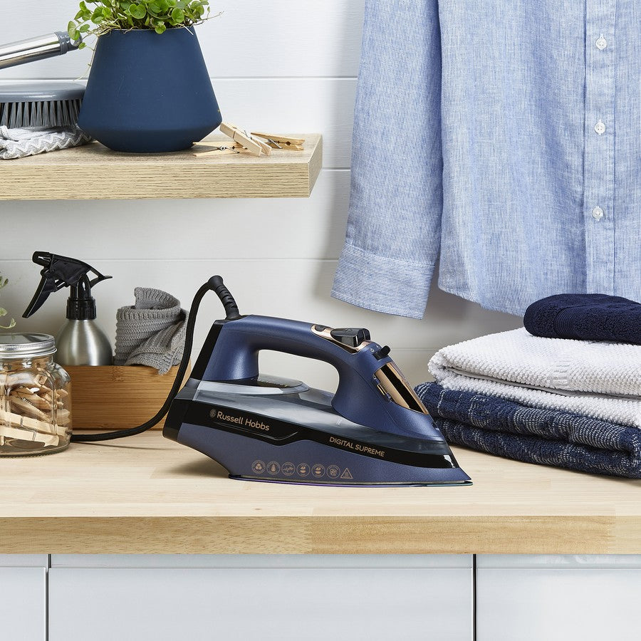 Russell Hobbs iron on a wooden surface with folded clothes and a shelf in the background