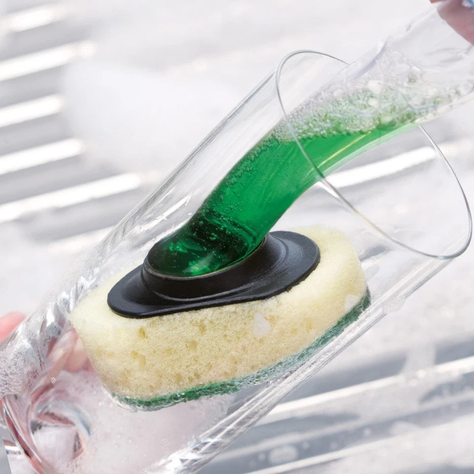 Green liquid being poured onto a white sponge with black center in a clear container.