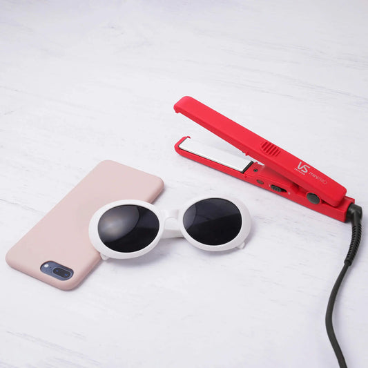 Red hair straightener, white sunglasses, and pink phone case on a light gray background